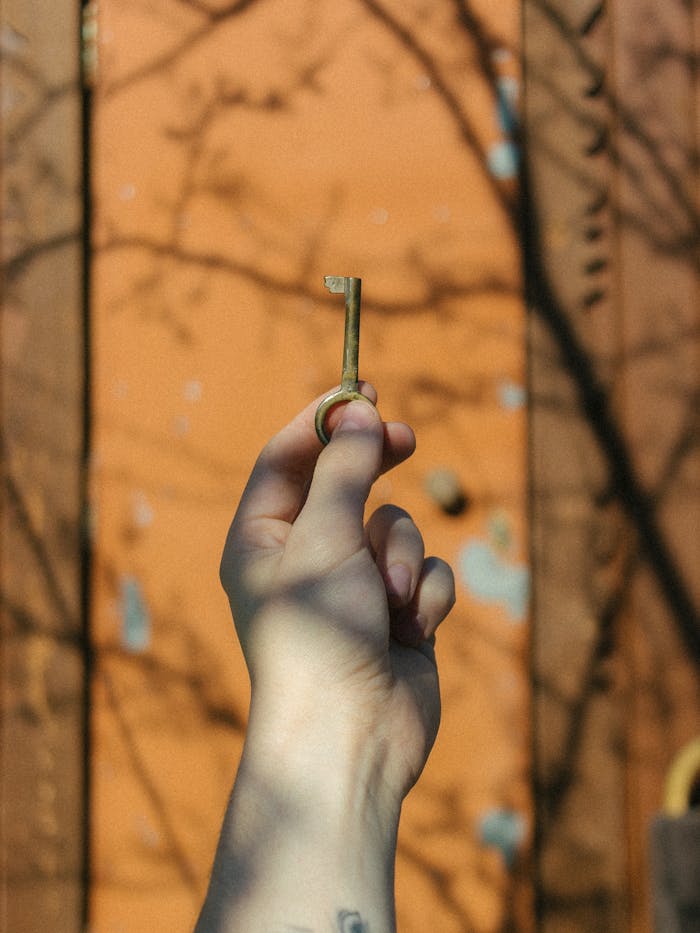 Home A hand holds an antique key against a rustic orange wooden door with shadows enhancing the scene.